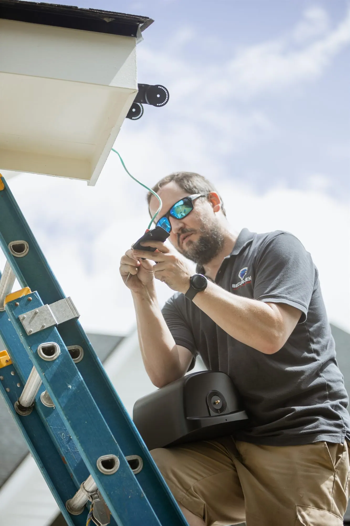 A technician on a ladder wiring a camera under an eave.