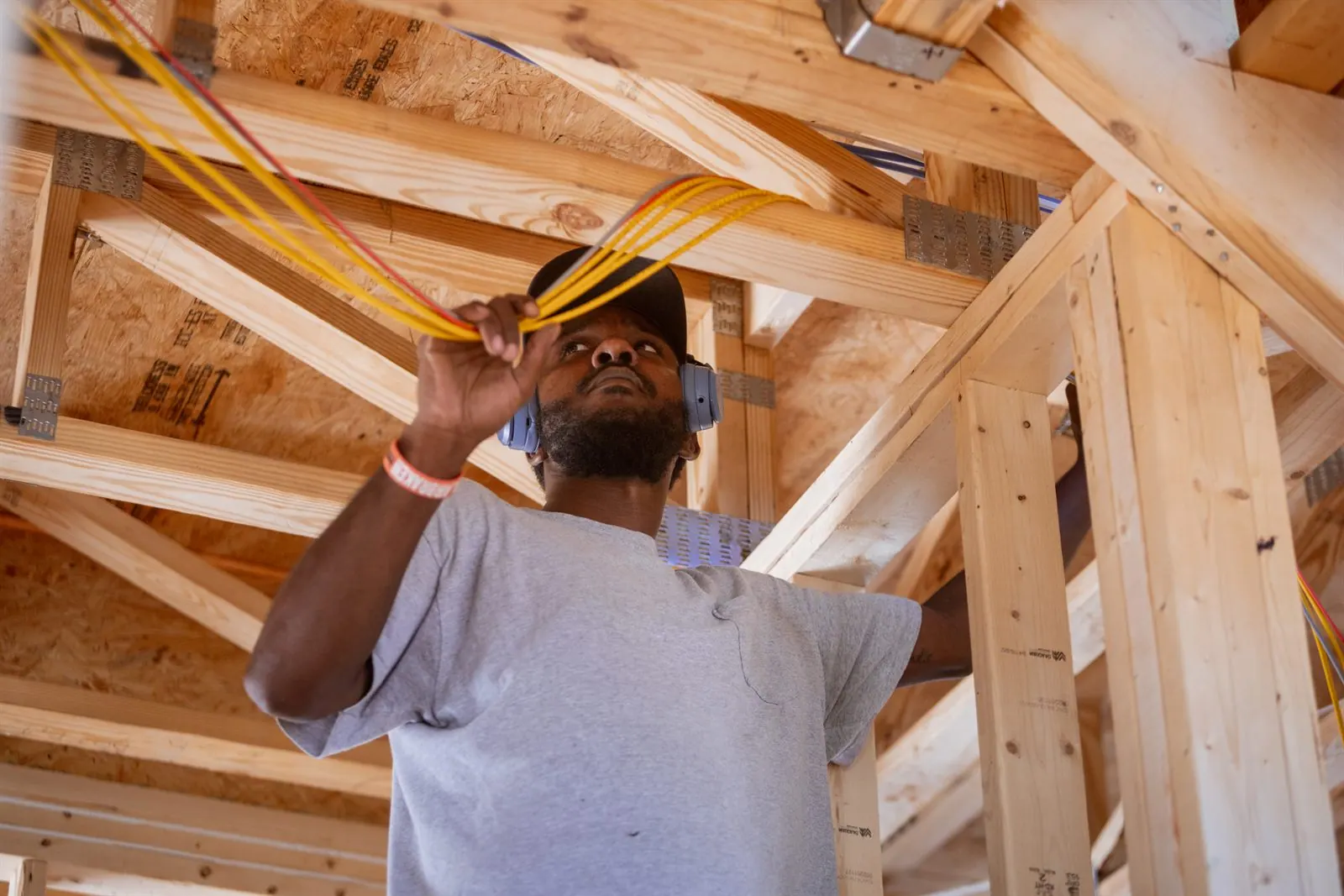A technician pulling cable through the trusses of a new build.